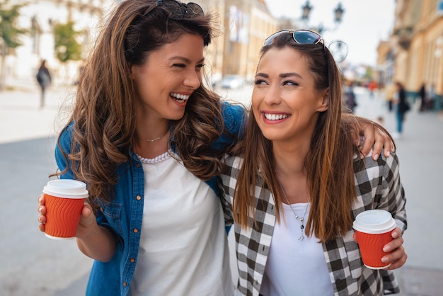 Foto retrato ao ar livre de duas meninas alegres bebendo café. caminhando na cidade.