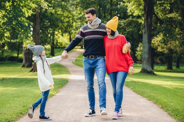 Retrato ao ar livre de família afetuosa caminhada no parque usar roupas de malha quentes Jovem bonito mantém a mão da filha parece com expressão feliz em seu conceito de descanso e relaxamento