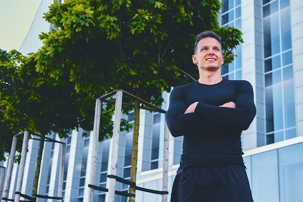 Retrato ao ar livre de homem atraente e atlético vestido com um sportswear preto sobre fundo de construção moderna.