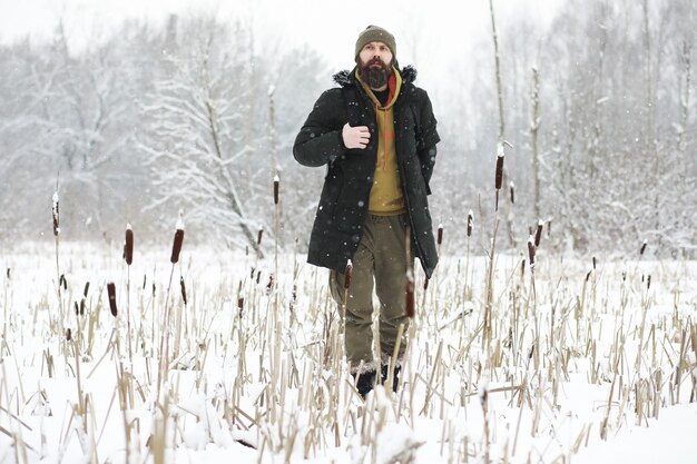 Retrato ao ar livre de homem bonito com casaco e casco. Homem barbudo na floresta de inverno.