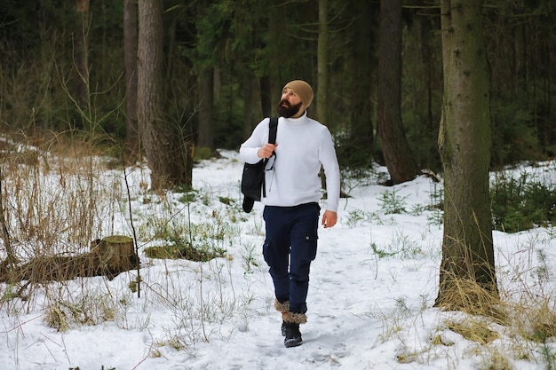 Retrato ao ar livre de homem bonito com casaco e casquinha. Homem barbudo na floresta de inverno.