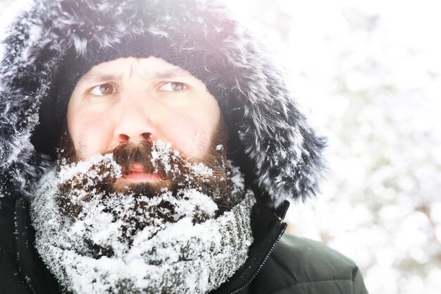 Retrato ao ar livre de homem bonito com casaco e casquinha. Homem barbudo na floresta de inverno.