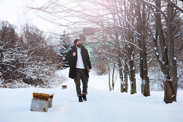 Retrato ao ar livre de homem bonito de casaco e scurf. Homem barbudo na floresta de inverno.