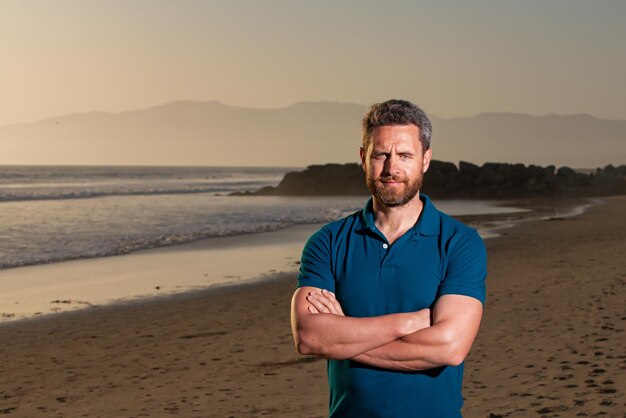 Retrato ao ar livre de homem bonito posando na incrível praia tropical em dia ensolarado de verão vestindo camiseta casual