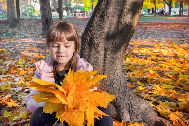 Retrato ao ar livre de outono de uma criança com um buquê de folhas de plátano amarelas em um parque ensolarado da cidade