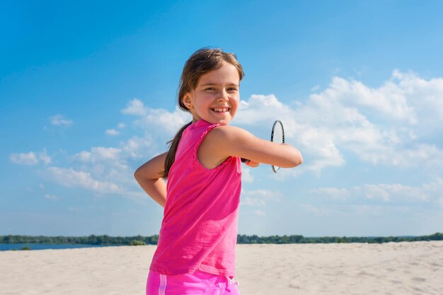 Retrato ao ar livre de uma garota feliz jogando badminton de praia na praia estilo de vida esportivo de férias de verão