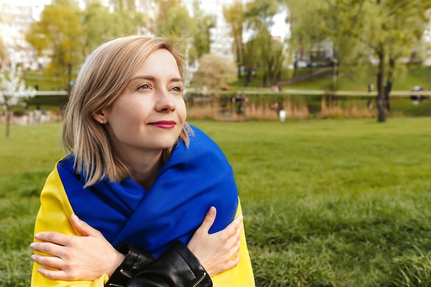 Retrato ao ar livre de uma jovem feliz com a bandeira da Ucrânia ao ar livre no parque da cidade O conceito de liberdade