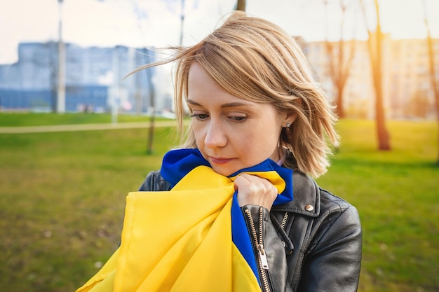 Retrato ao ar livre de uma jovem triste com uma bandeira da Ucrânia ao ar livre em um parque da cidade
