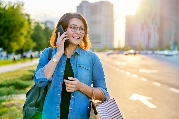 Retrato ao ar livre de uma linda mulher de 40 anos falando no telefone com sacolas de compras