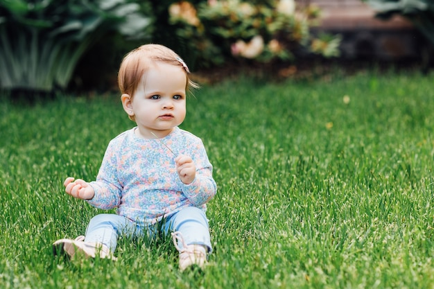 Retrato ao ar livre de uma menina bonitinha em uma bela roupa localizada na grama do jardim