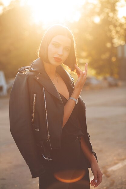Retrato ao ar livre de uma modelo bronzeada sedutora vestindo jaqueta preta, posando em uma rua