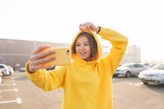 Retrato ao ar livre de uma mulher elegante em roupas de rua faz selfie.