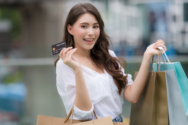 Retrato ao ar livre de uma mulher feliz segurando sacolas de compras com cartão de crédito e um rosto sorridente no shopping