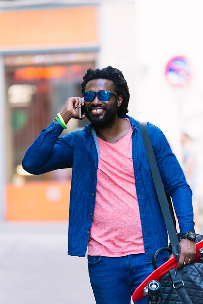 Retrato ao ar livre do jovem Africano bonito usando o celular na rua.