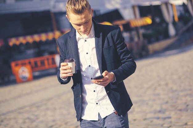 Retrato ao ar livre do jovem moderno com telefone celular na rua.