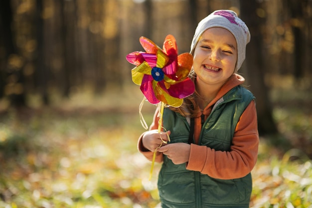 Retrato ao ar livre do outono de uma linda criança feliz na floresta com bastão de moinho de vento
