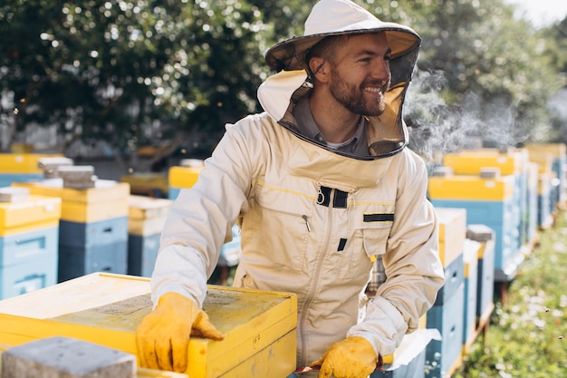 Foto retrato de un apicultor masculino feliz que trabaja en un apiario cerca de colmenas con abejas recoger miel apicultor en apiario concepto de apicultura