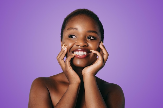 Foto retrato aproximado da bela modelo africana negra nua com pele impecável tocando suas bochechas isoladas sobre fundo roxo cosméticos de beleza cuidados com a pele