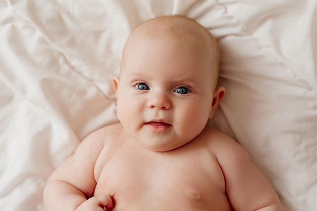 Retrato aproximado de um bebê recém-nascido de olhos azuis deitado de costas em um lençol branco feliz despreocupado