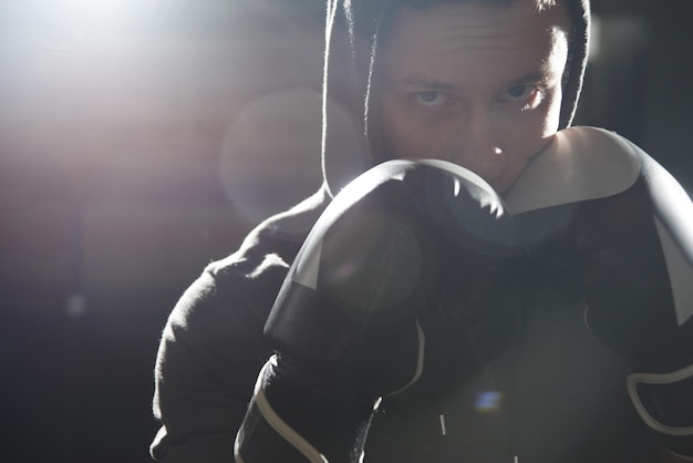 Retrato aproximado de um boxeador profissional legal em luvas e um capuz olhando agressivamente para a câmera batendo com o punho