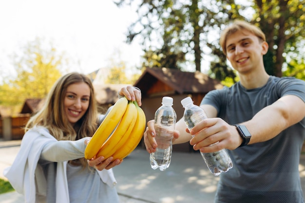 Retrato aproximado de um homem e uma menina saudáveis segurando frutas de banana e água