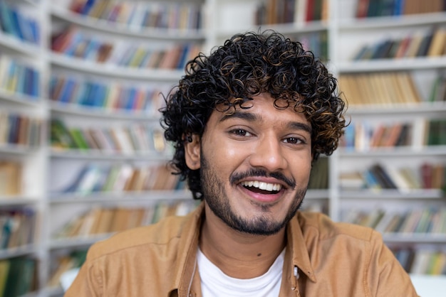 Retrato aproximado de um jovem estudante hispânico com cabelo encaracolado sorrindo e olhando para a câmera jovem