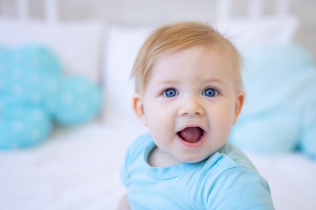 Retrato aproximado de um pequeno bebê loiro sorrindo com olhos azuis em casa na cama