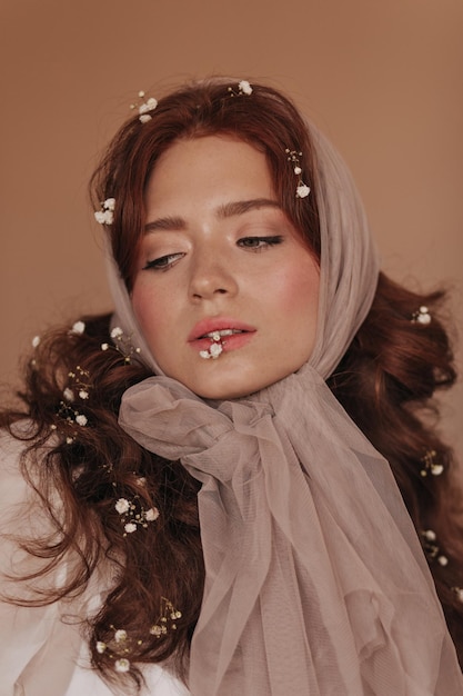 Retrato aproximado de uma jovem com sardas e lenço de chiffon na cabeça posando com flores brancas no cabelo