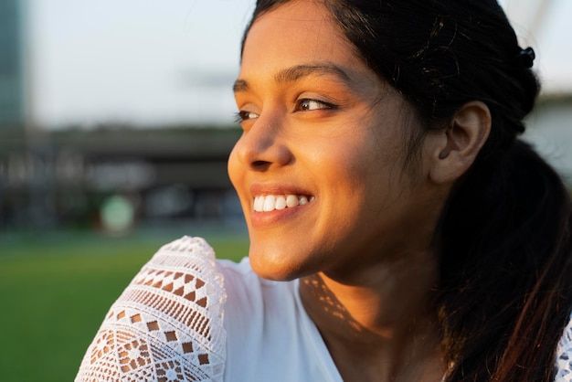 Retrato aproximado de uma linda mulher indiana sorridente aproveitando o dia ensolarado olhando para longe sentado no parque