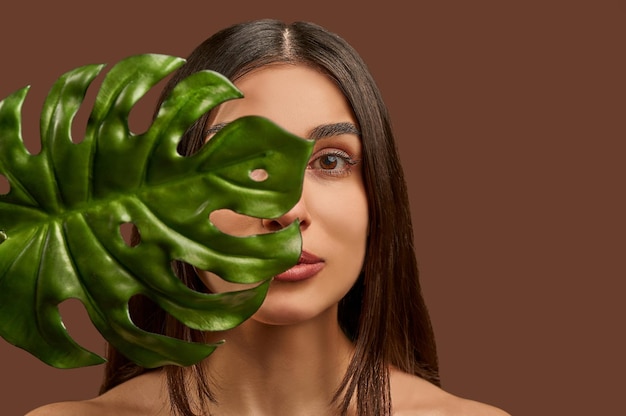 Retrato aproximado de uma linda mulher segurando um galho de uma planta de monstros escondendo seu rosto