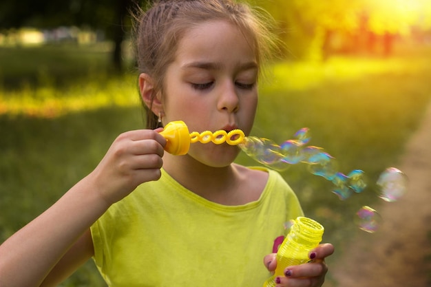 Retrato aproximado de uma menina bonitinha com bolhas de sabão em um dia ensolarado