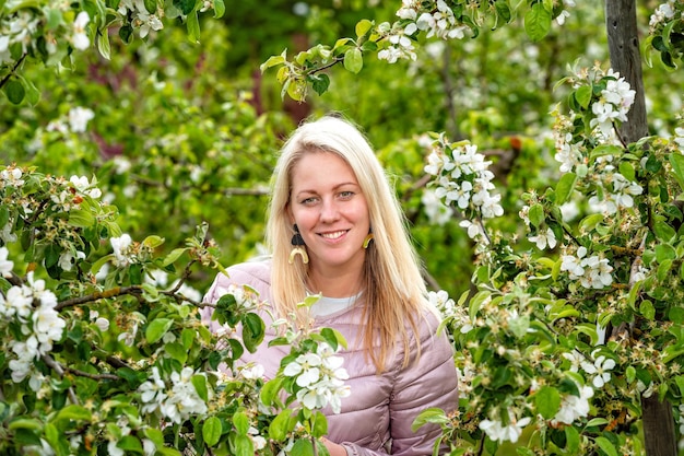 Retrato aproximado de uma mulher loira sorridente em um jardim florescente em foco seletivo de primavera