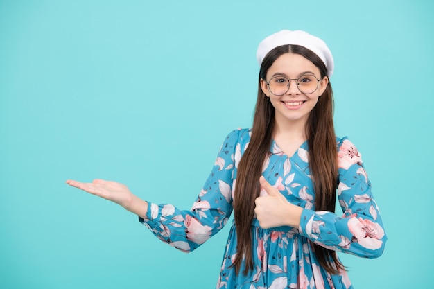 Retrato aproximado dela, ela é uma garota bonita, atraente e alegre, espantada, apontando para o lado no espaço da cópia, isolado no fundo azul Adolescente feliz, emoções positivas e sorridentes