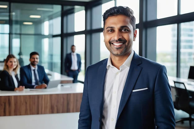 Retrato de un apuesto empresario asiático indio sonriente jefe en un traje de pie en su oficina de la compañía de negocios moderna sus trabajadores de pie en el fondo borroso
