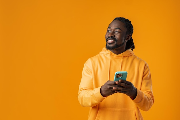 Retrato de un apuesto hombre africano usando su móvil contra un fondo amarillo