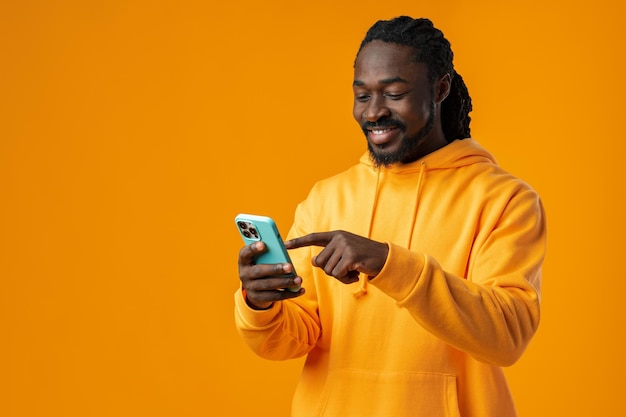 Retrato de un apuesto hombre africano usando su móvil contra un fondo amarillo