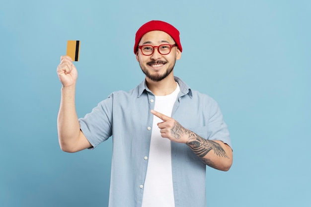 Retrato de un apuesto hombre asiático sonriente con anteojos hipster rojos y elegantes con tarjeta de crédito