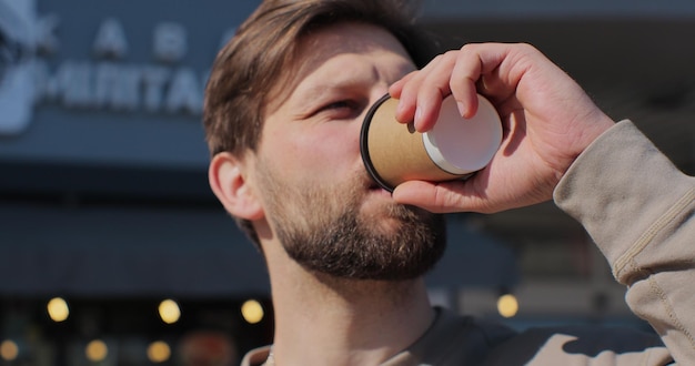 Retrato de un apuesto hombre barbudo sosteniendo una taza de café para llevar y sonriendo parado en la calle en un buen día tomando café