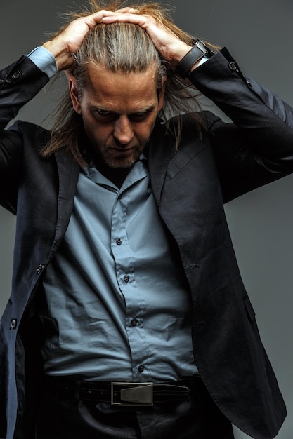 Retrato de un apuesto hombre elegante de pelo largo con traje gris oscuro. Aislado sobre fondo gris.