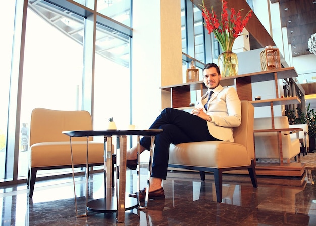 Retrato de un apuesto hombre exitoso bebiendo café sentado en una cafetería hombre de negocios desayunando en el vestíbulo del hotel