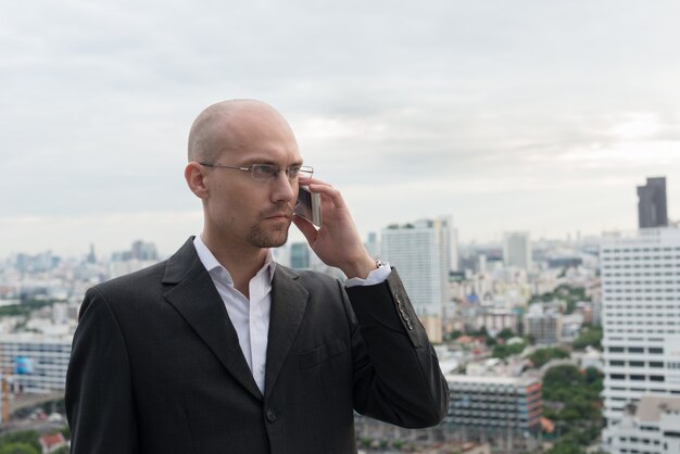 Retrato de apuesto hombre de negocios calvo con rastrojo de barba contra la vista de la ciudad al aire libre