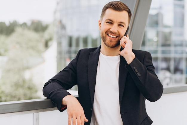 Retrato de un apuesto hombre de negocios feliz con traje hablando por teléfono en el fondo de edificios urbanos y oficinas