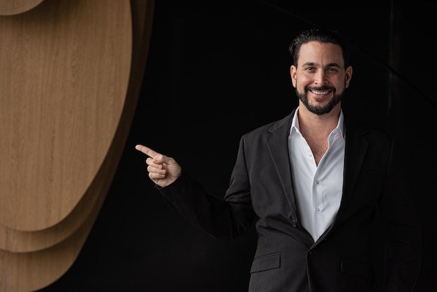 Foto retrato de un apuesto hombre de negocios con fondo negro señalando con el dedo para copiar el espacio