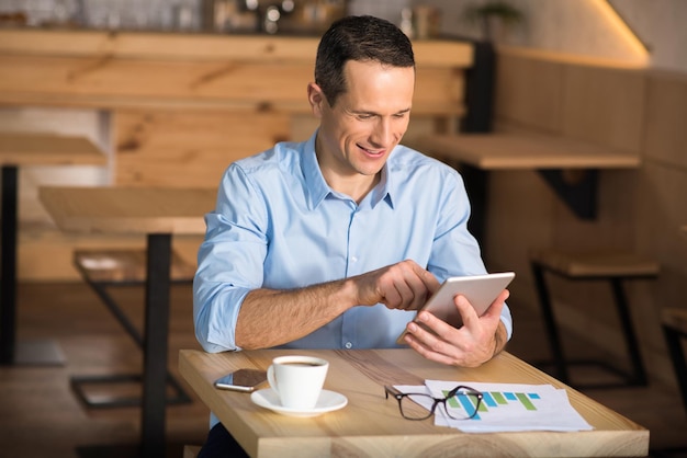 Retrato de un apuesto hombre de negocios sonriente usando una tableta digital en el café