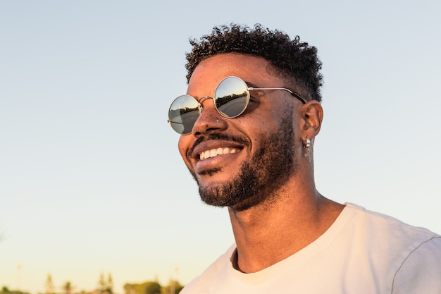 Retrato de un apuesto hombre negro americano con gafas de sol durante la puesta de sol en la playa.