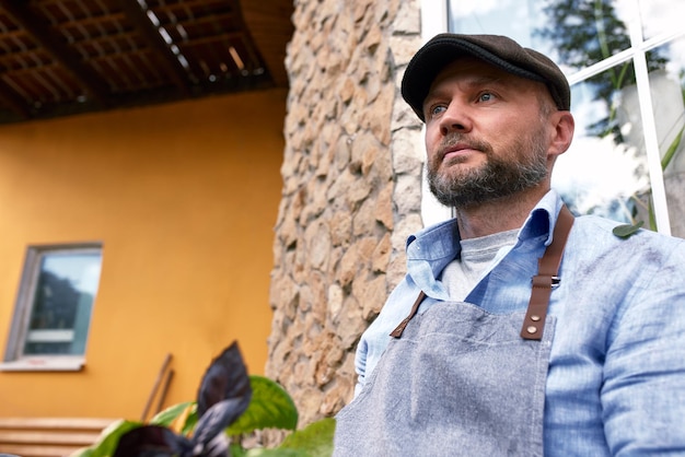 Retrato de un apuesto jardinero con sombrero sostiene hojas de lechuga Jardinería orgánica El concepto de cosecha y agricultura local