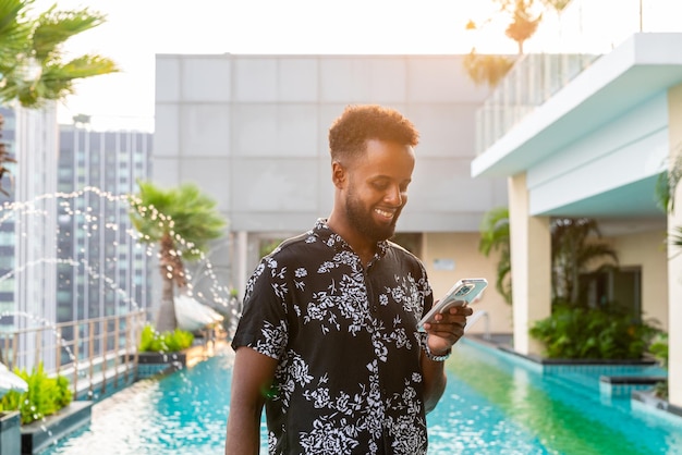 Retrato de un apuesto joven africano al aire libre usando un teléfono móvil