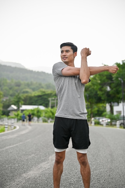 Foto retrato de un apuesto joven asiático estirando los brazos y el cuerpo antes de correr