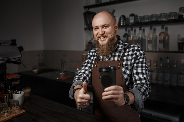 Retrato de un apuesto joven barista en delantal sentado en el bar del café moderno