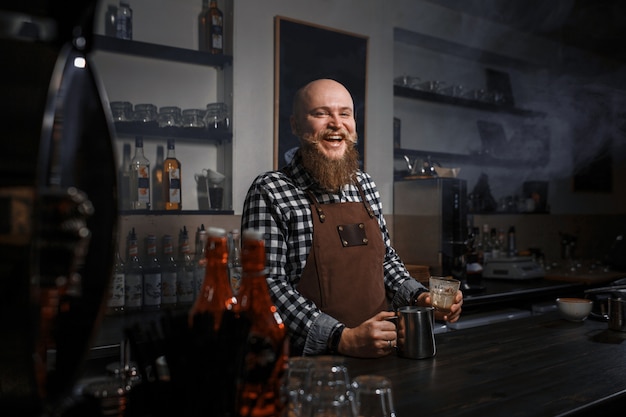 Retrato de un apuesto joven barista en delantal sentado en el bar del café moderno